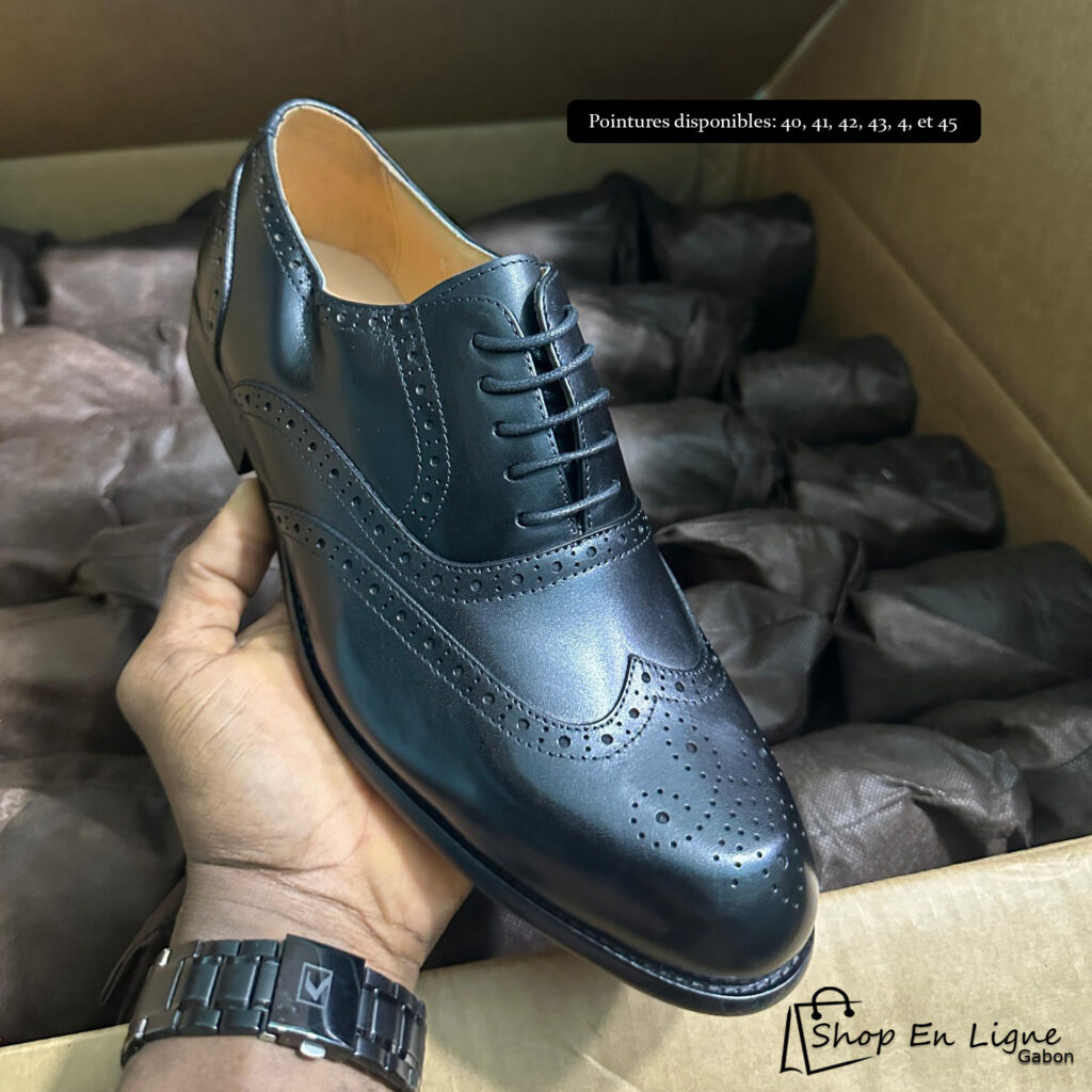 Chaussure Richelieu brogue noire pour homme avec perforations décoratives de style bout fleuri, présentée sur fond de colis de livraison Shop En Ligne Gabon.