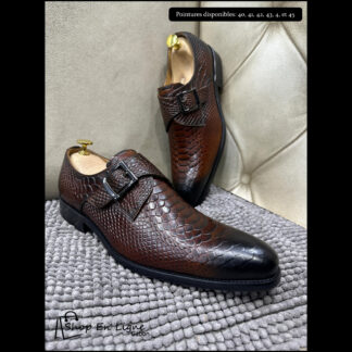 Paire de chaussures Monk pour homme en cuir marron motif écailles avec patine noire au bout et boucle métallique, posée sur un tapis gris.