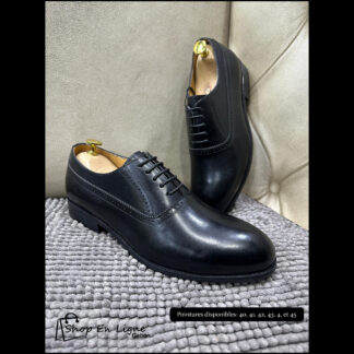 Chaussures de ville Oxford homme en cuir noir brillant avec détails perforés, disposées sur un tapis gris.