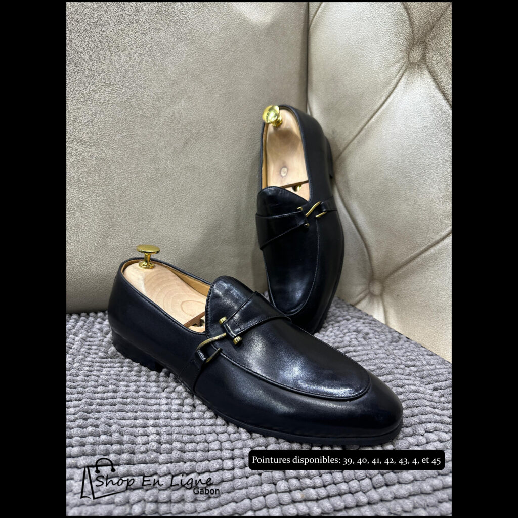 Mocassins de luxe pour homme en cuir noir lisse avec détail boucle dorée, posés sur un tapis gris.