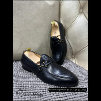 Mocassins de luxe pour homme en cuir noir lisse avec détail boucle dorée, posés sur un tapis gris.